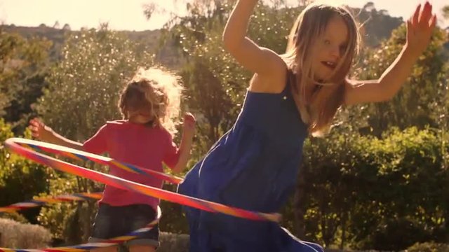 Slow motion two children playing with hula hoop in park.