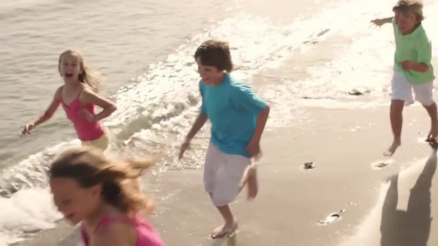 Slow motion of five children running on beach.