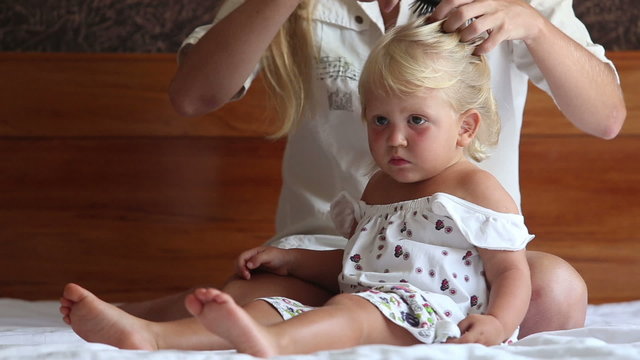 mother plaits hair to small daughter watching cartoon	