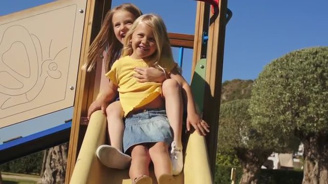 Slow motion of two children on slide in park.