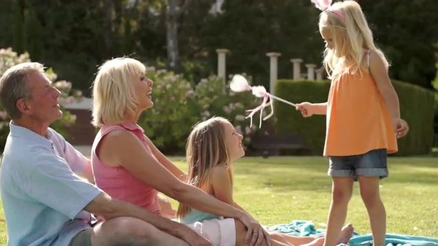 Grandparents and two granddaughters playing in park with magic wand.