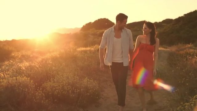 Slow motion of young couple walking on sand dunes in sunset.