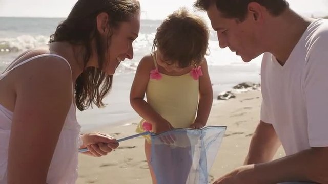 Parents and daughter with fishing net at the beach.