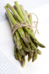 Asparagus Tied with Twine – Spears of asparagus tied up with twine. On a light blue striped background.