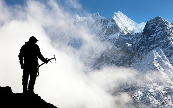 Silhouette of man with ice axe in hand and mountains