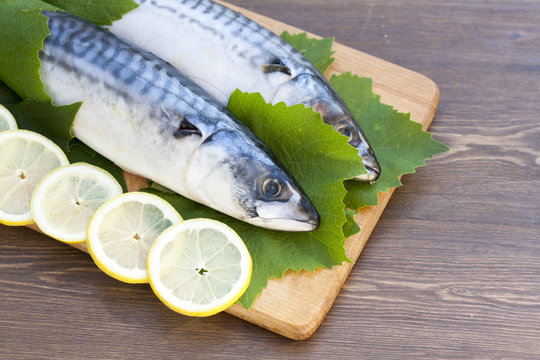Fresh mackerel in grape leaves with lemon slices in wooden table