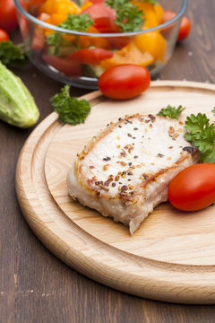 Fried pork steak with vegetables and parsley on a wooden board