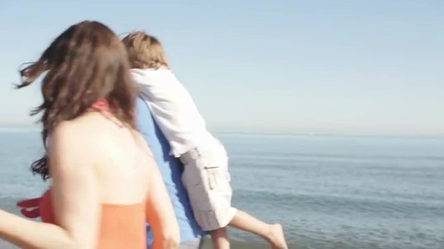 Slow motion of family running along beach and parents carrying children.