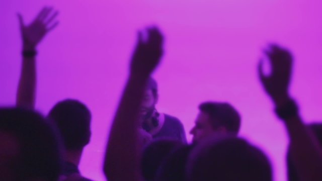 DJ working at night club, many people waving hands in euphoria