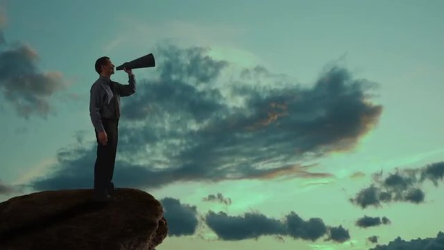 Businessman talking into a megaphone on a mountain. 