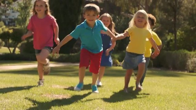 Tilt up slow motion shot of five children running towards camera in park.