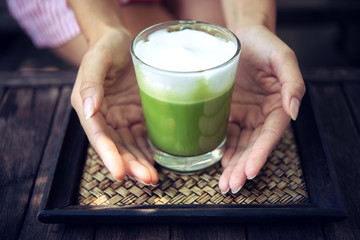 Woman holding Matcha green tea latte on wooden table