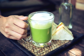 Woman holding Matcha green tea latte on wooden table