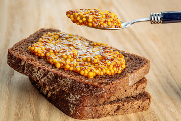 Wholegrain mustard spoon over bread slice