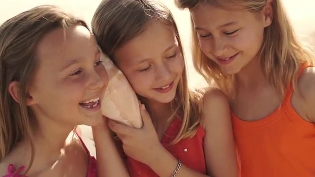 Three girls playing on beach listening to conch shell.