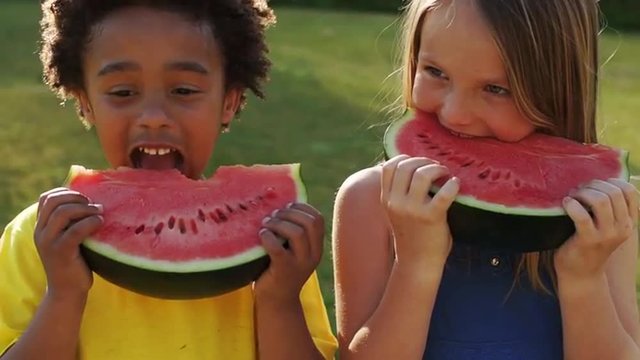 Slow motion of two children eating water melon in park