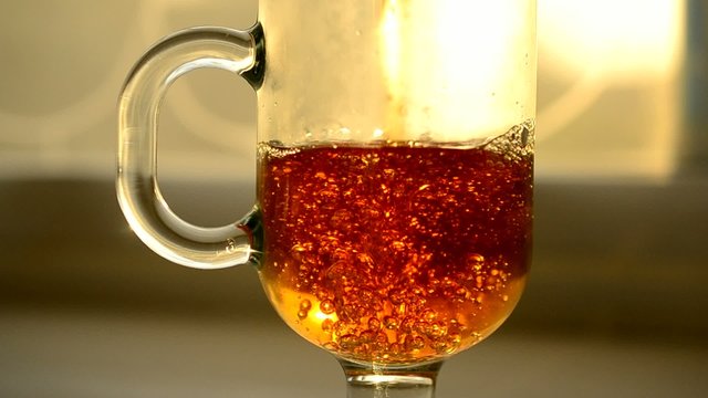 Pouring black tea into empty glass cup with bubbles and foam