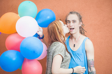 Young happy couple near the orange wall stand with balloons