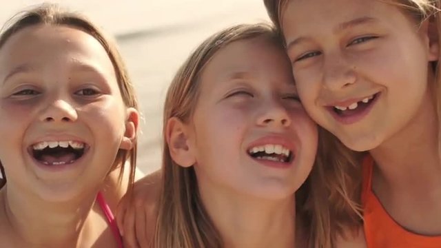Close up of three girls playing on beach laughing to camera.