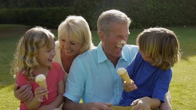 Grandparents and grandchildren sitting together in garden playing with ice cream.