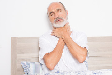Elderly man sitting on bed suffering from throat problems