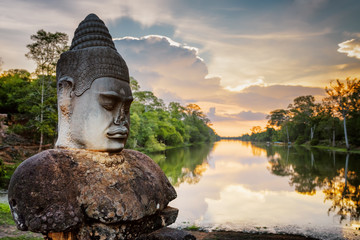 Stone Asura and sunset over moat surrounding Angkor in Cambodia - obrazy, fototapety, plakaty