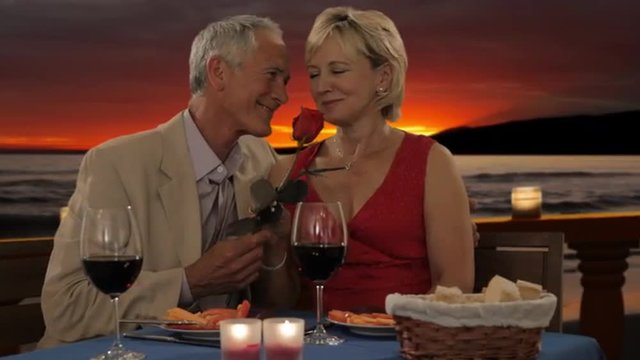 dolly shot of senior couple at dinner in sunset giving rose