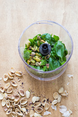 Ingredients for Pesto Sauce with Pistachio Nuts in a Plastic Bowl of Food Processor on Rustic Wooden Background