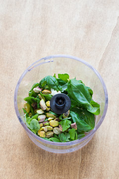 Ingredients for Pesto Sauce with Pistachio Nuts in a Plastic Bowl of Food Processor on Rustic Wooden Background