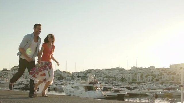 Slow motion shot of couple running by marina in sunset.