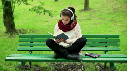 Girl listening music and reading book in the park
