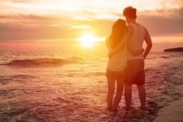 young couple watching sunset on the beach - Powered by Adobe