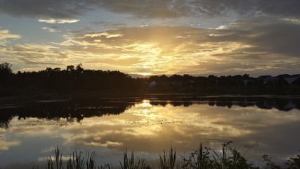 pond with setting sun and clouds reflected on water and grass on bank