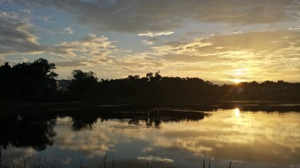 Fototapeta premium pond with setting sun and clouds reflected on water