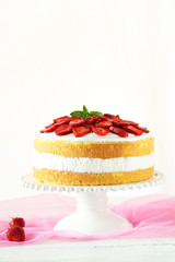Sweet cake with strawberries on cake stand on white wooden backg