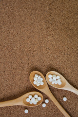 pills in a wooden spoon on a cork background.