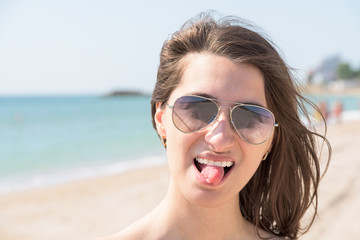 Portrait Of Happy Young Woman Sticking Out Tongue On Beach