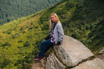 Naklejka na ściany i meble Young woman sitting on a cliff and enjoying a view of mountains