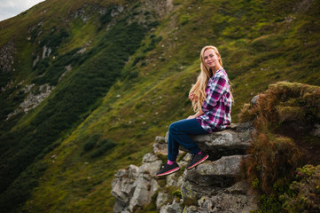 Naklejka na ściany i meble Young woman sitting on a cliff and enjoying a view of mountains