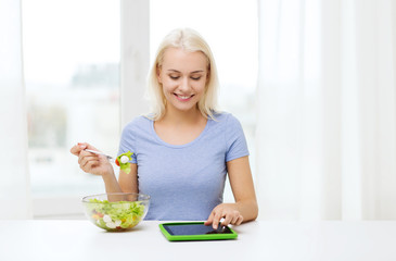 smiling woman eating salad with tablet pc at home