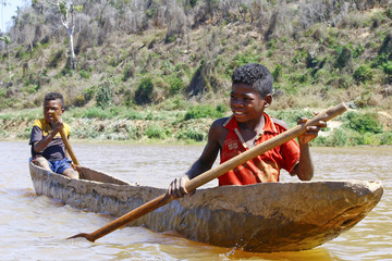 Young Malagasy african boy rowing traditional canoe on river - obrazy, fototapety, plakaty