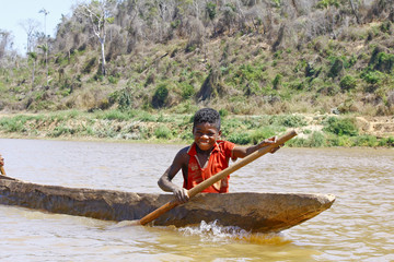 Young Malagasy african boy rowing traditional canoe on river