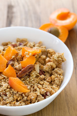 granola with fruits and nuts in white bowl on brown wooden background