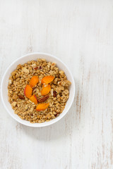 granola with apricot and nuts in white bowl on white wooden background