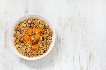 granola with apricot and nuts in white bowl on white wooden background