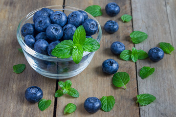 Blueberries in a bowl decorated with mint, on a wooden table