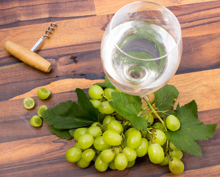 Grüne Weintrauben mit Weinglas und Korkenzieher auf Holzuntergrund