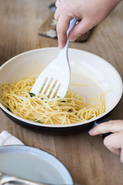 Hands Mixing Spaghetti with Melted Butter and Fried Sage Leaves in a Ceramic Pan