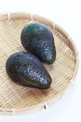 Two avocado fruit in bamboo tray on white background