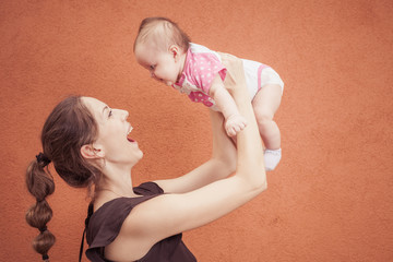 Happy young mother throw up baby on a background of orange wall. Child laughs in flight. Girl three...